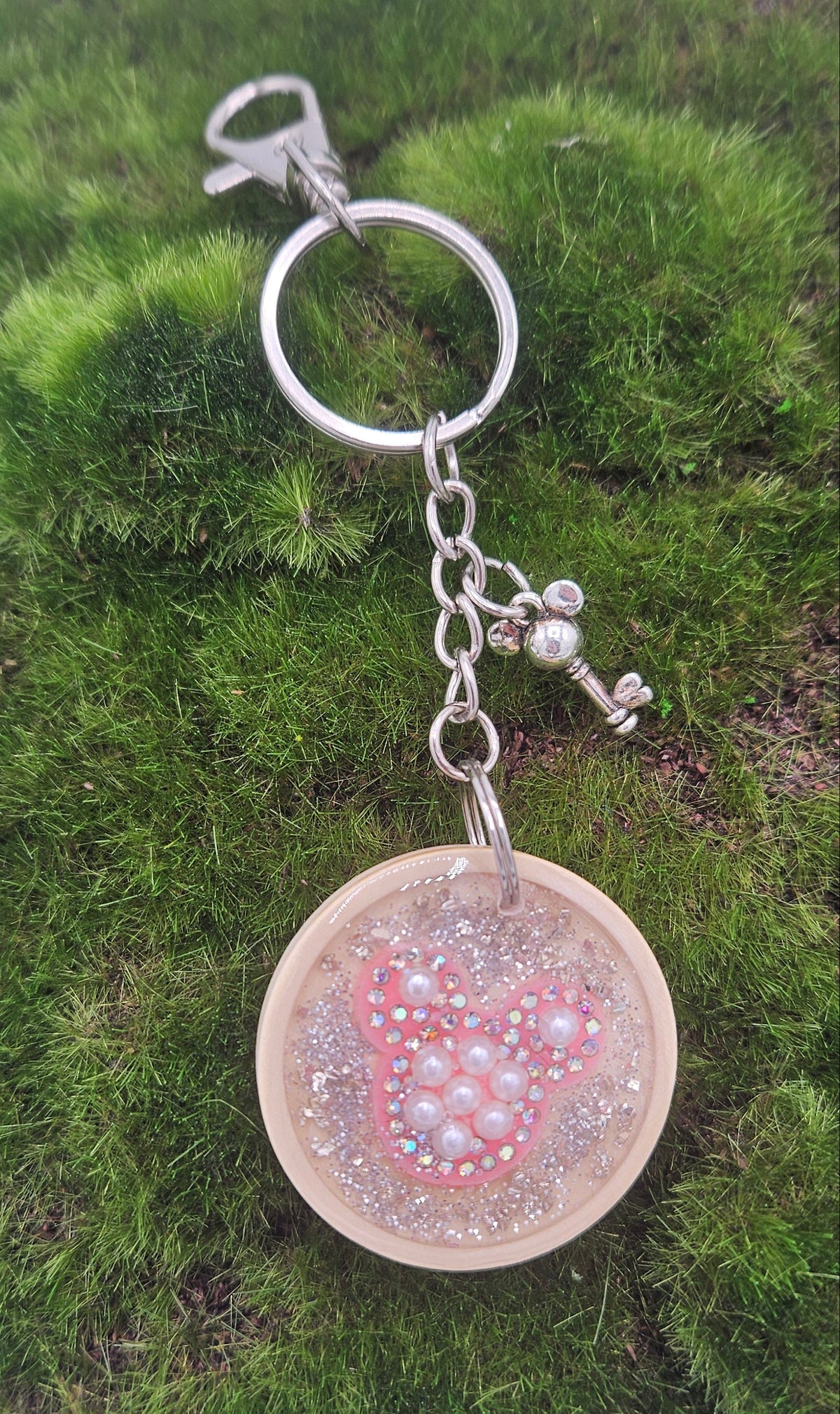 A silver keychain with a round wooden charm containing a pink glittery hidden mouse head design